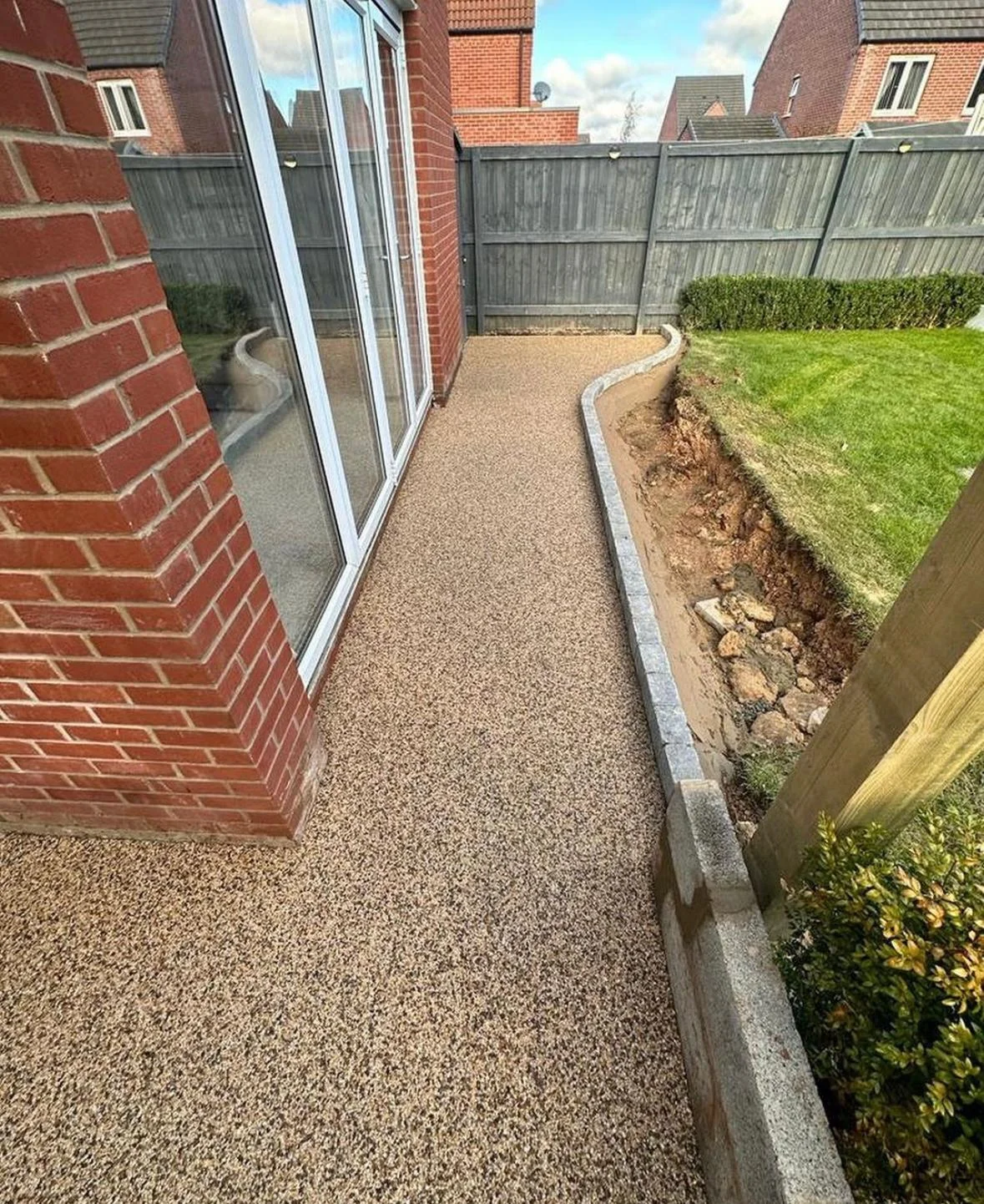 Golden resin path following a raised garden edge beside a brick house